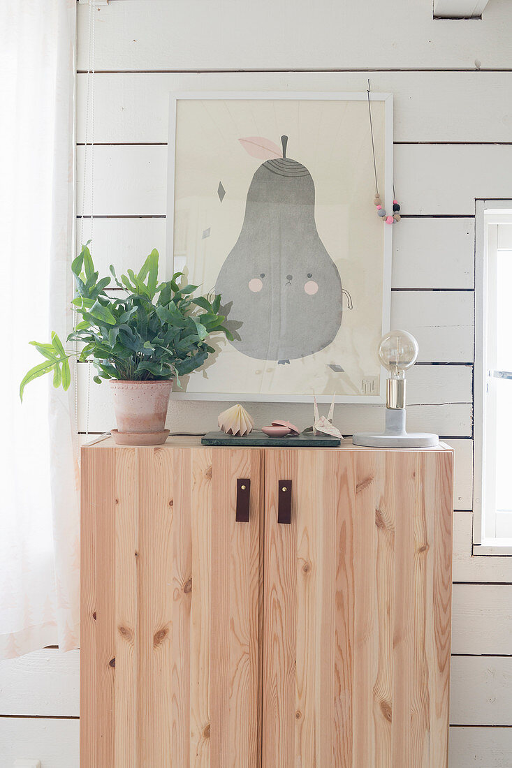 Niedliches Birnen-Bild überm Holzschränkchen mit Leder-Laschen