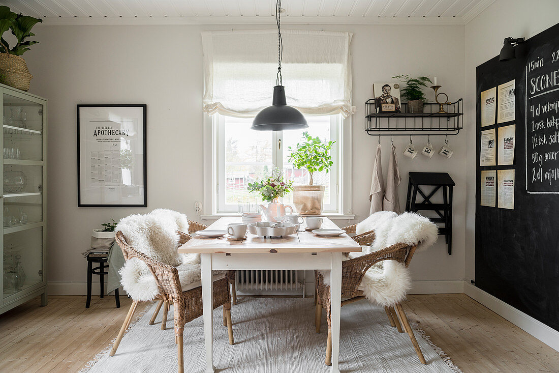 Fur rugs on wicker chairs around set table in dining room with chalkboard wall