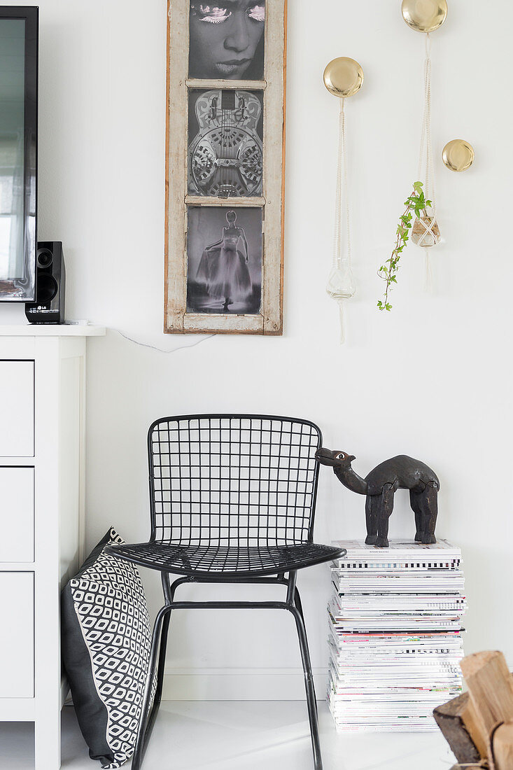 Schwarzer Metallstuhl und Zeitschriftenstapel unterm alten Fenster als Bilderrahmen