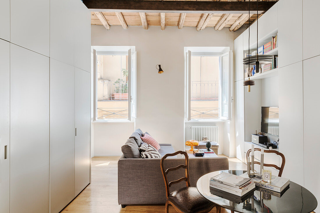 Kleiner Wohnraum mit Sofa, rundem Esstisch und Küche versteckt im weißen Einbauschrank