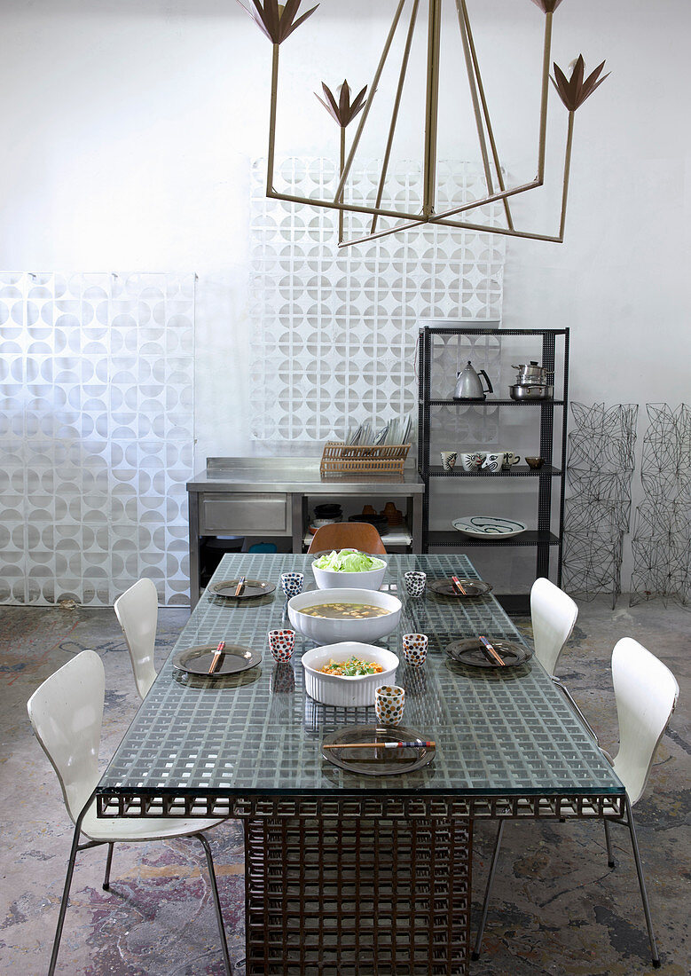 Iron, brass-effect designer chandelier above iron mesh table in artist's studio apartment
