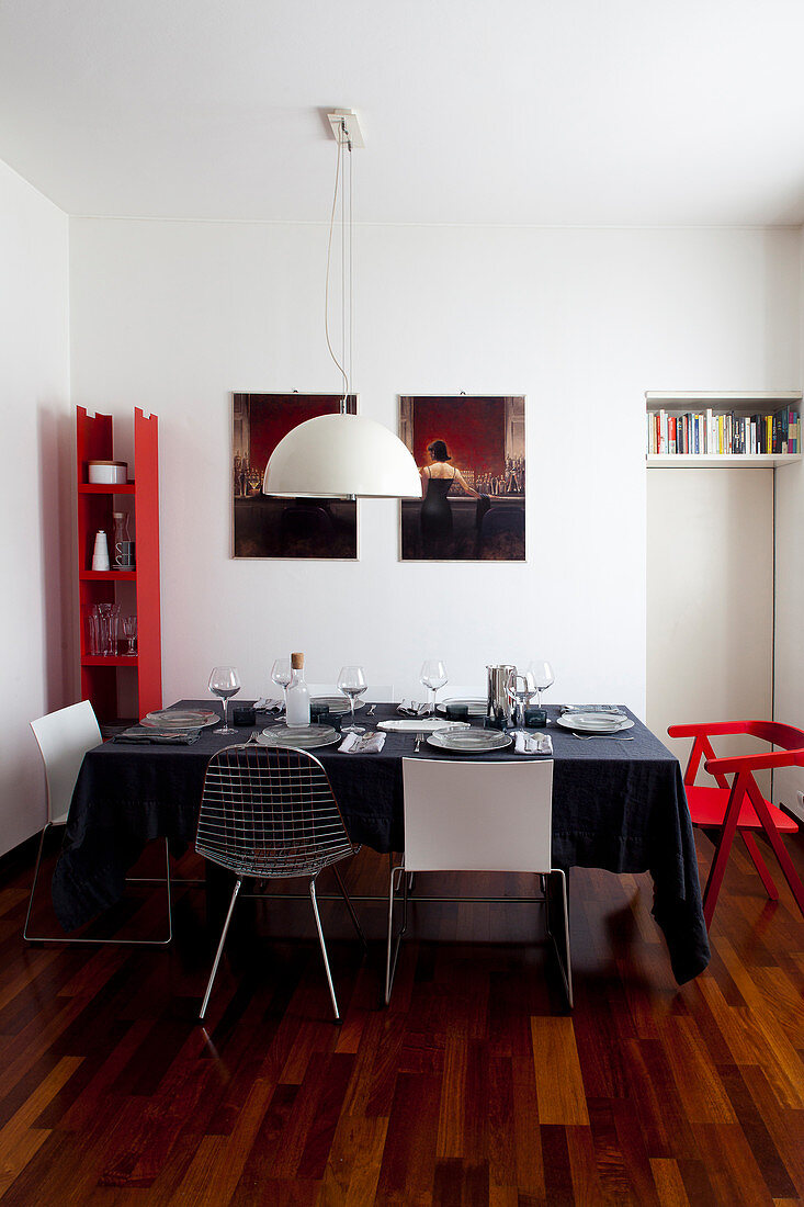 Gedeckter Esstisch mit schwarzer Tischdecke in Wohnraum mit weißen Wänden und roten Farbakzenten