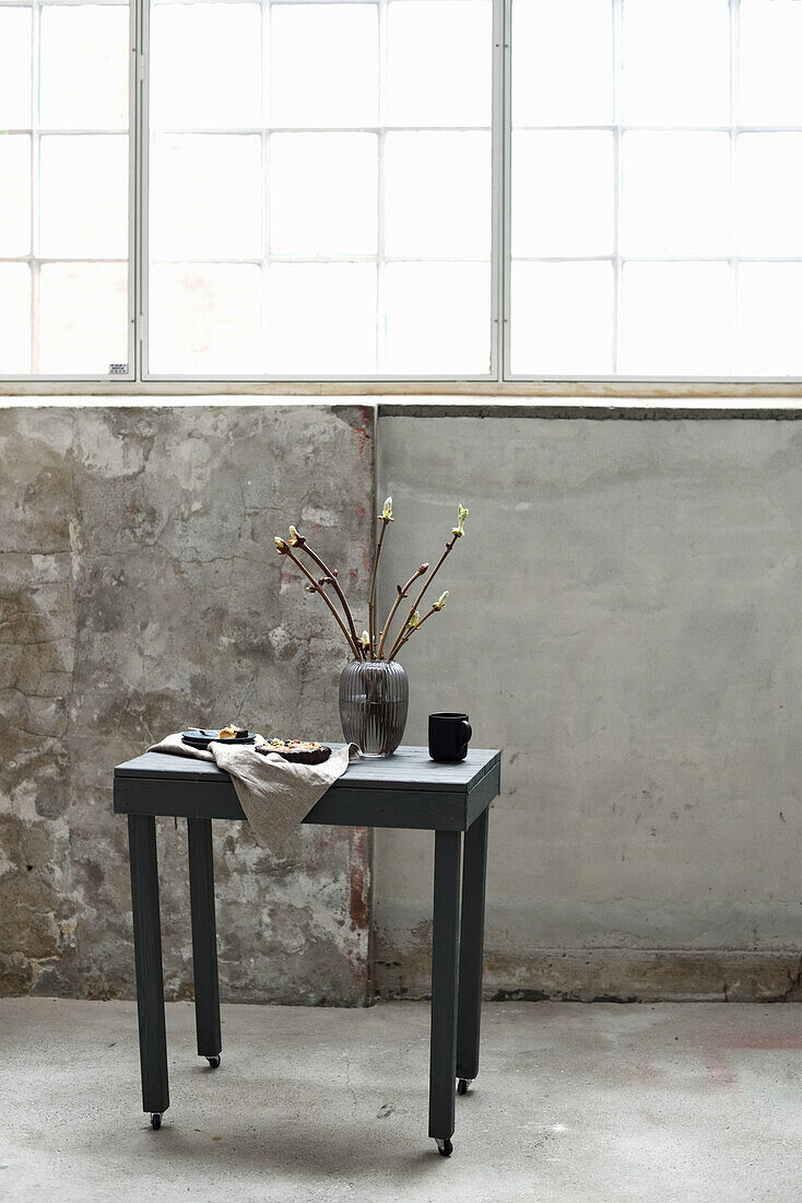 Table with vase and cake in front of concrete wall