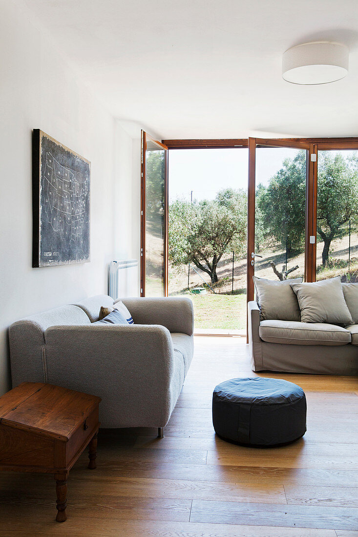 Wohnzimmer mit grauen Sofas und geöffneten Terrassentüren mit Blick auf toskanische Landschaft