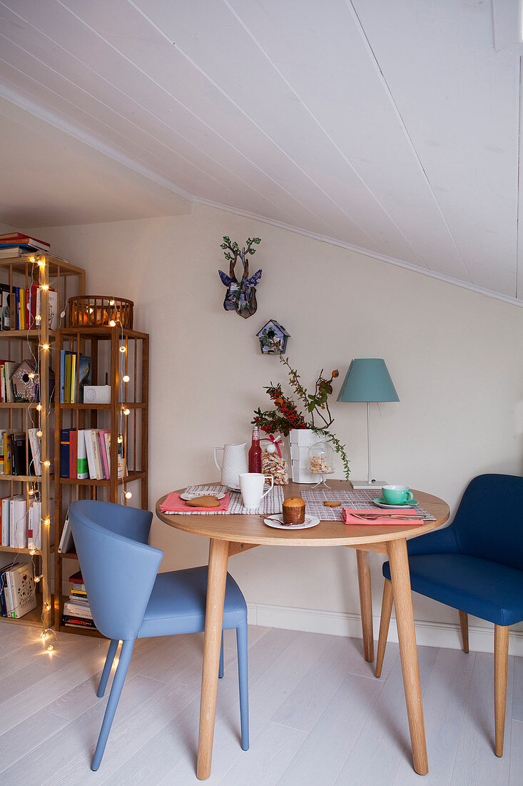 Runder Kaffeetisch mit blauen Stühlen in weihnachtlich dekoriertem Raum unter Dachschräge