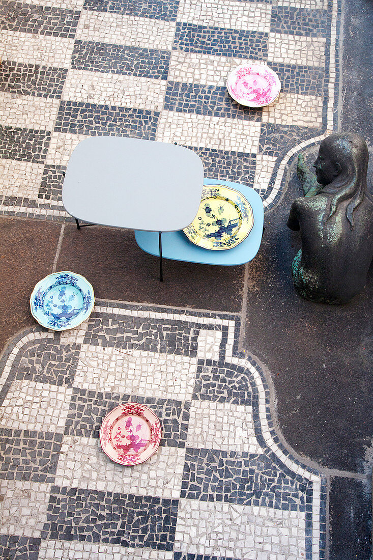 Sitzende Frauen-Bronzestatue neben Designertisch und italienischen Dekortellern auf Mosaikboden