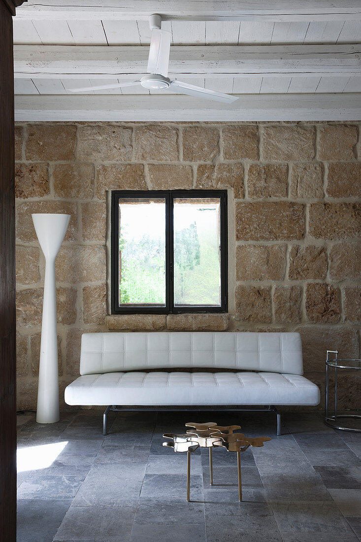 Modernes weißes Sofa mit Designer-Stehleuchte vor rustikaler Natursteinwand