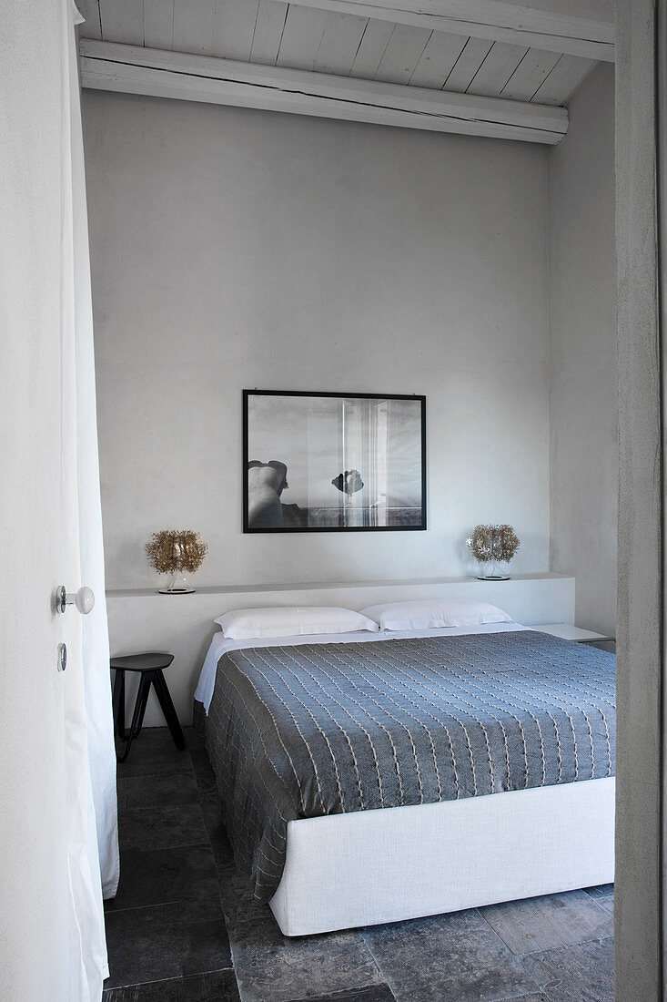 Schlicht gehaltenes Schlafzimmer in Grau- und Weißtönen mit Doppelbett und Wandbild