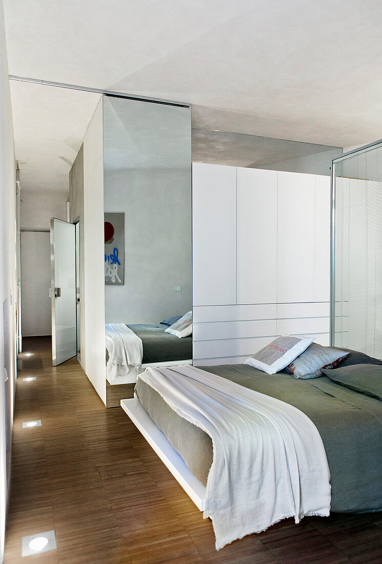 Open-plan bedroom with glass partition as headboard and floor-to-ceiling mirror