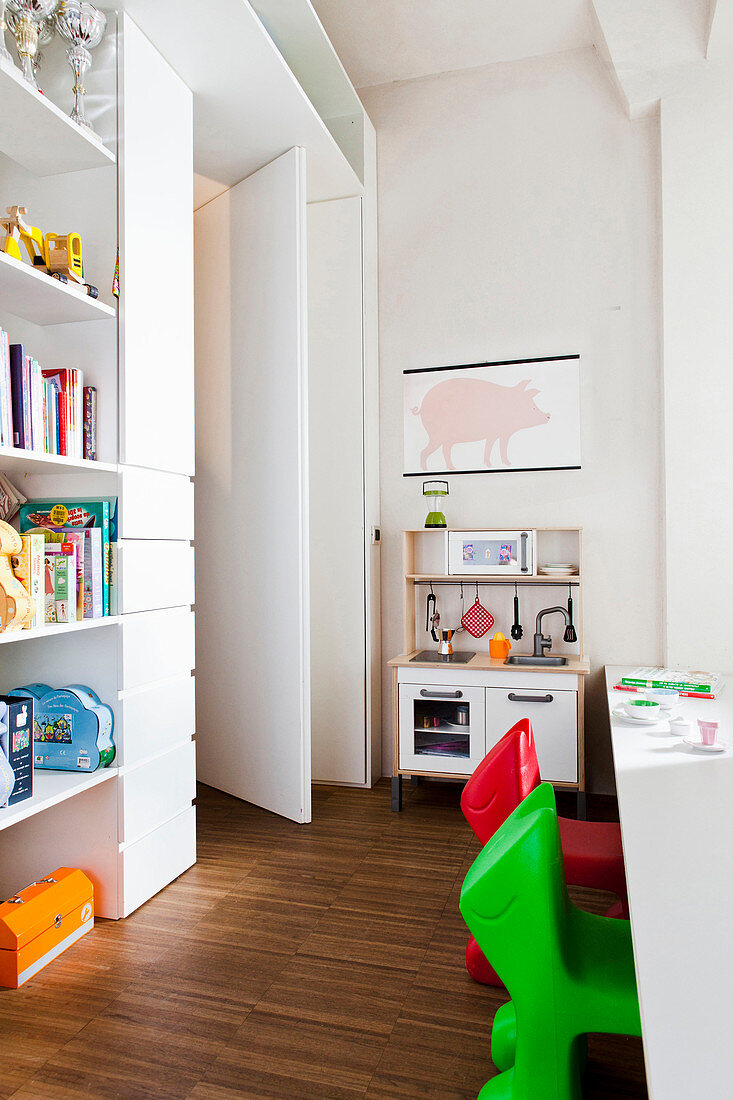 Kinderzimmer mit Spielzeugküche, Wandregalen und bunten Kinderstühlen vor Spieltisch