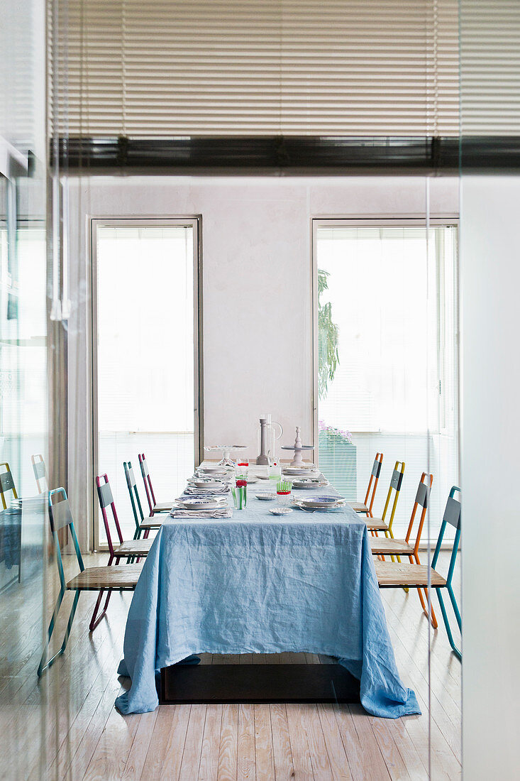 Blick auf Esstisch für viele Personen mit blauer Tischdecke und bunten Stahlrohrstühlen