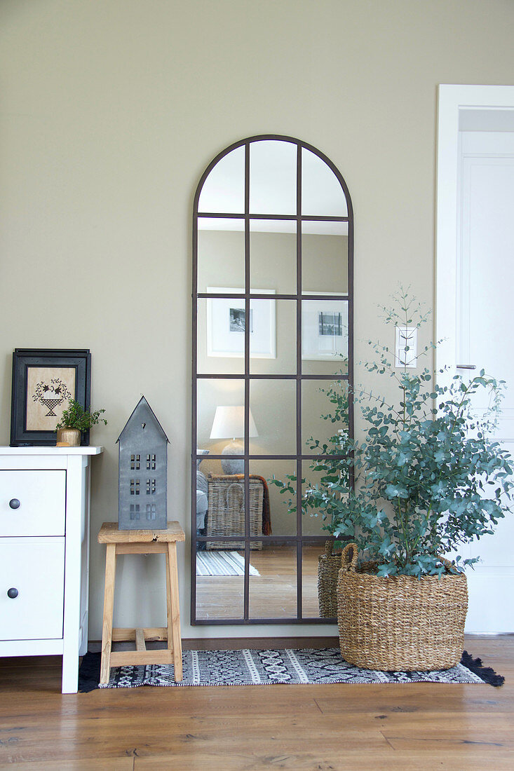 Arched, lattice mirror on wall and eucalyptus planted in basket in living room