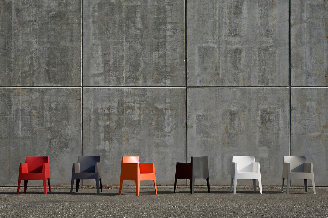 Plastic chairs in various colours on road in front of concrete façade