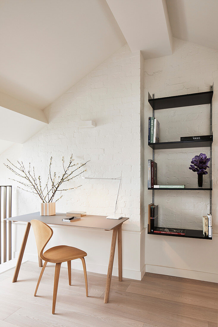 Desk and chair against whitewashed brick wall and black wall-mounted shelves
