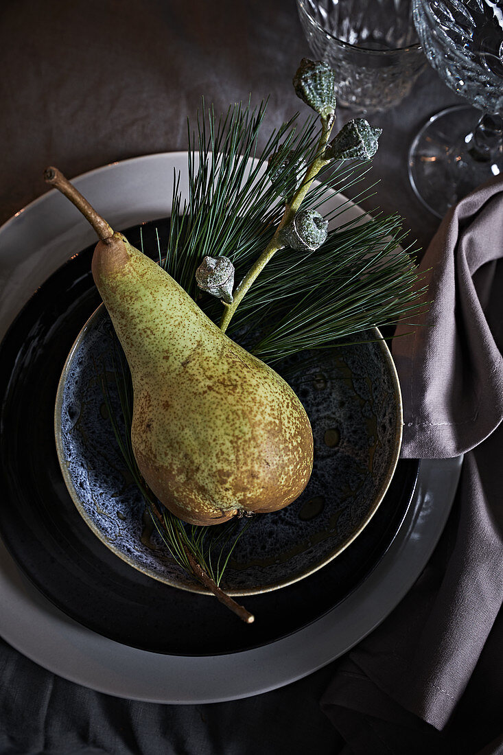 Place setting festively decorated with pear and sprigs of eucalyptus and pine