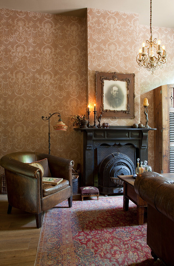 Vintage leather armchairs in front of black fireplace in living room of period building with patterned wallpaper