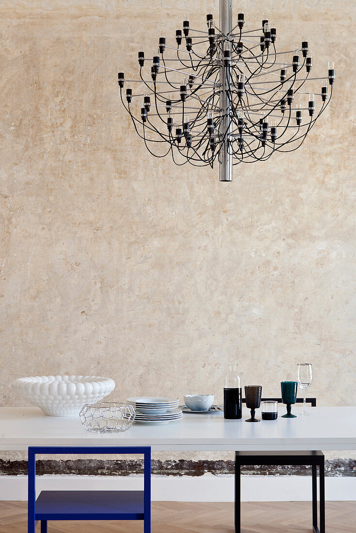 Modern chandelier above dining table in front of patinated wall