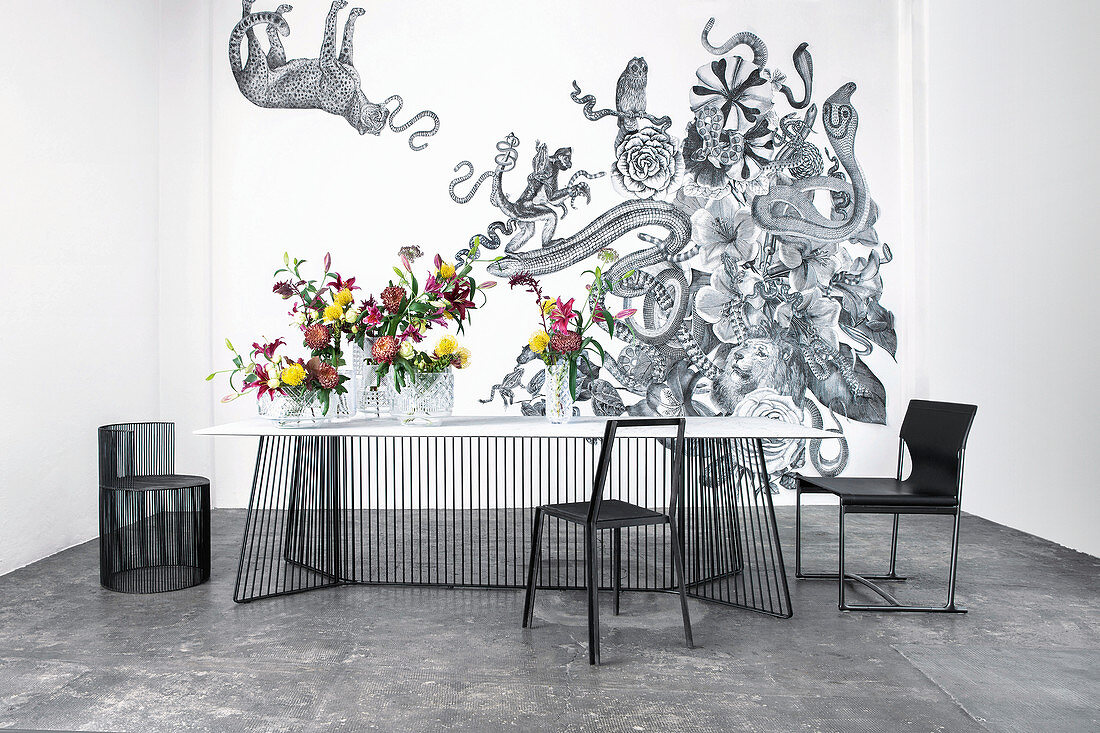 Delicate dining table and black chairs in front of exotic wallpaper