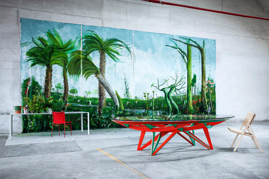 Red and green designer table in front of huge painting of jungle