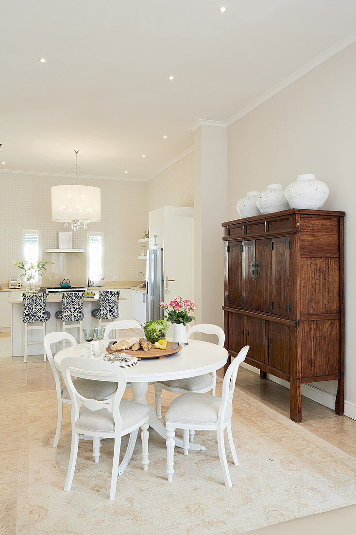 Round white dining table and antique-style upholstered chairs with kitchen counter in background