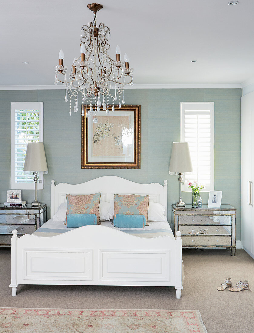 Weißes Holzbett in elegantem Schlafzimmer mit Kronleuchter und taubengrauen Wänden