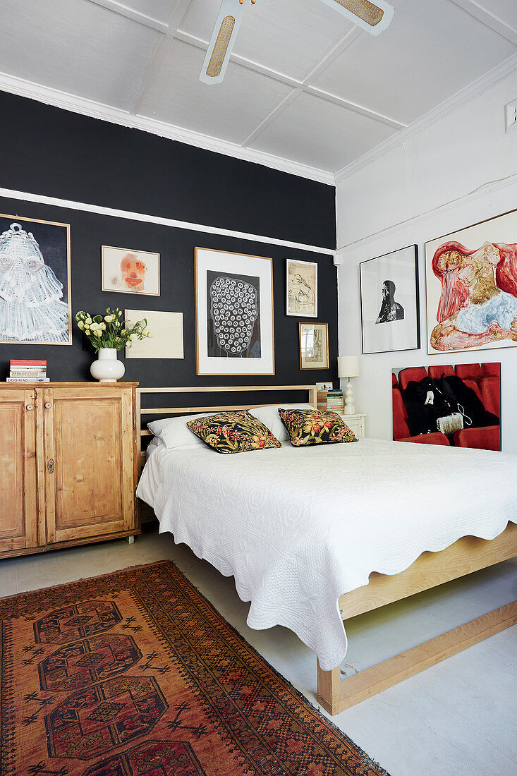 Schlafzimmer mit Holzbett und Bildergalerie an schwarzen und weißen Wänden