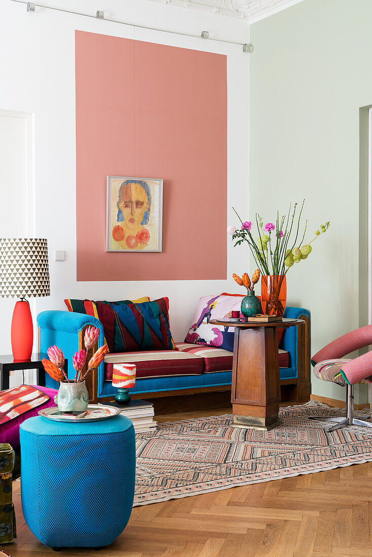 Pouf und Daybed mit blauen Farbakzenten, Holztisch und rosa Wandfläche im Wohnzimmer