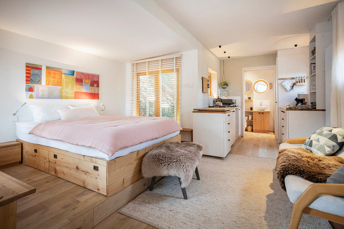 Doppelbett auf Holzpodest, dahinter Küchenbereich und Durchgang zum Bad in Tiny House