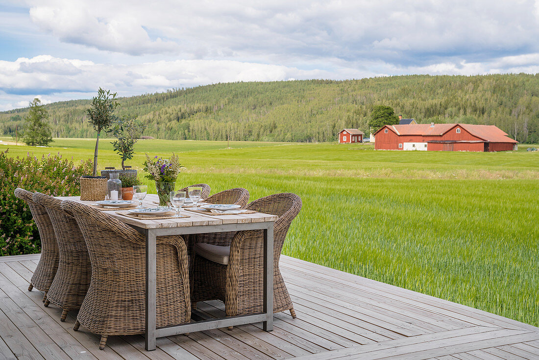 Table and wicker chairs on deck with view of fields and woods