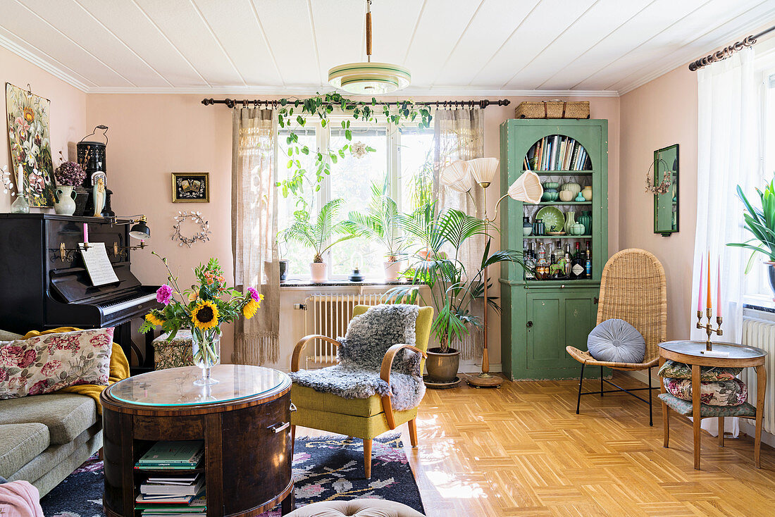 Runder Tisch, Sessel, Klavier und grüner Vitrinenschrank im Wohnzimmer mit rosa Wänden