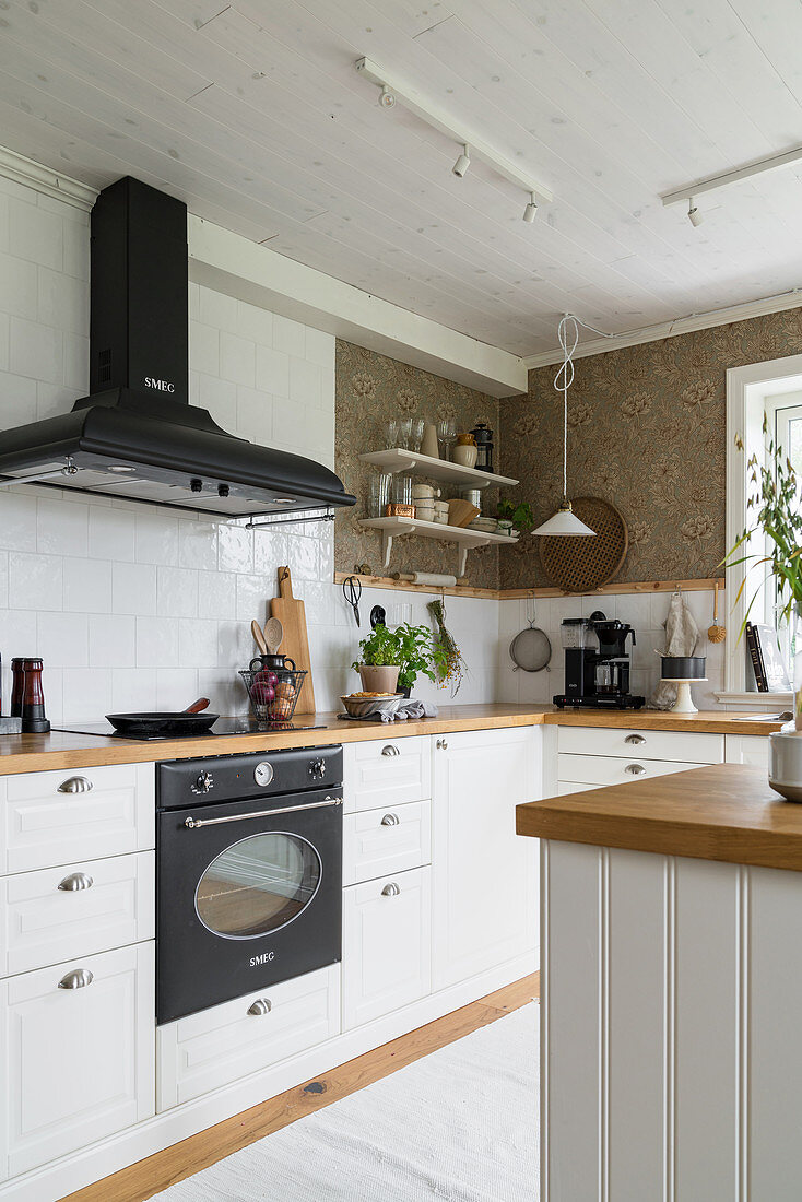 Kitchen in classic country-house style with white cabinets, white tiled splashback and floral wallpaper