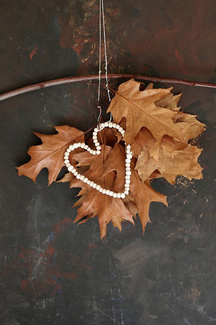 Zusammengeknüpfte getrocknete Eichenblätter mit Perlenherz als Herbstdekoration