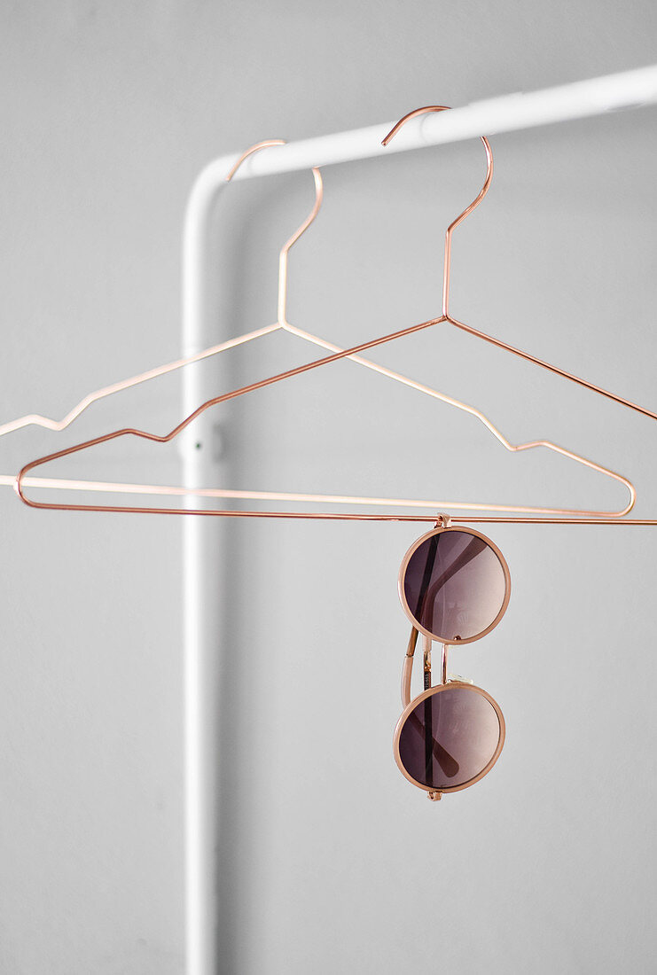 Sunglasses hanging from coat hanger on clothes rail