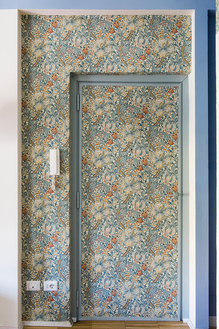 Tür und Nischenbereich tapeziert mit floraler Mustertapete in Blau- und Orangetönen