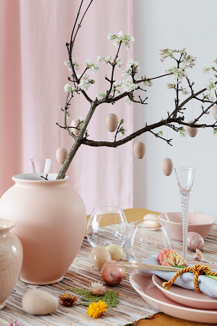 Wooden eggs hung from flowering branch in vase on Easter table set in pink