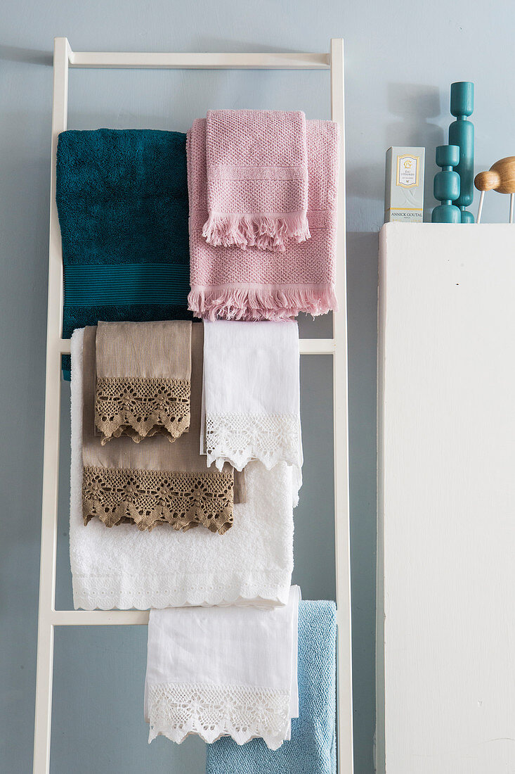 Towels of various colours with fringes and lace trim hung on towel rack