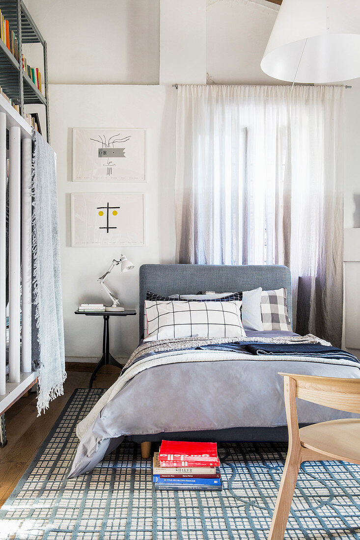 Bed with upholstered headboard and grey bed linen on blue-and-white patterned rug