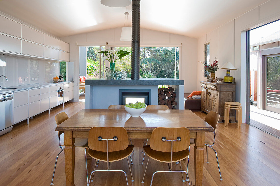 Esstisch mit Stühlen und Kamin vor weißer Küchenzeile in offenem Wohnraum