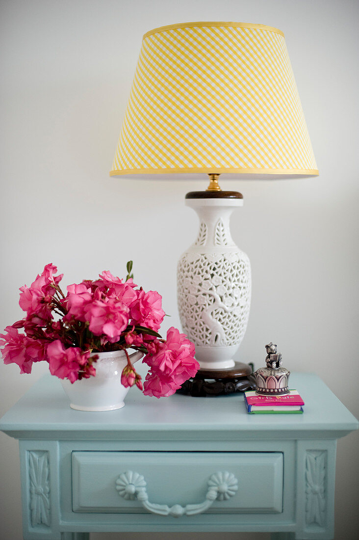 Tischlampe mit Keramikfuß und pinkfarbene Blumen auf Nachttisch