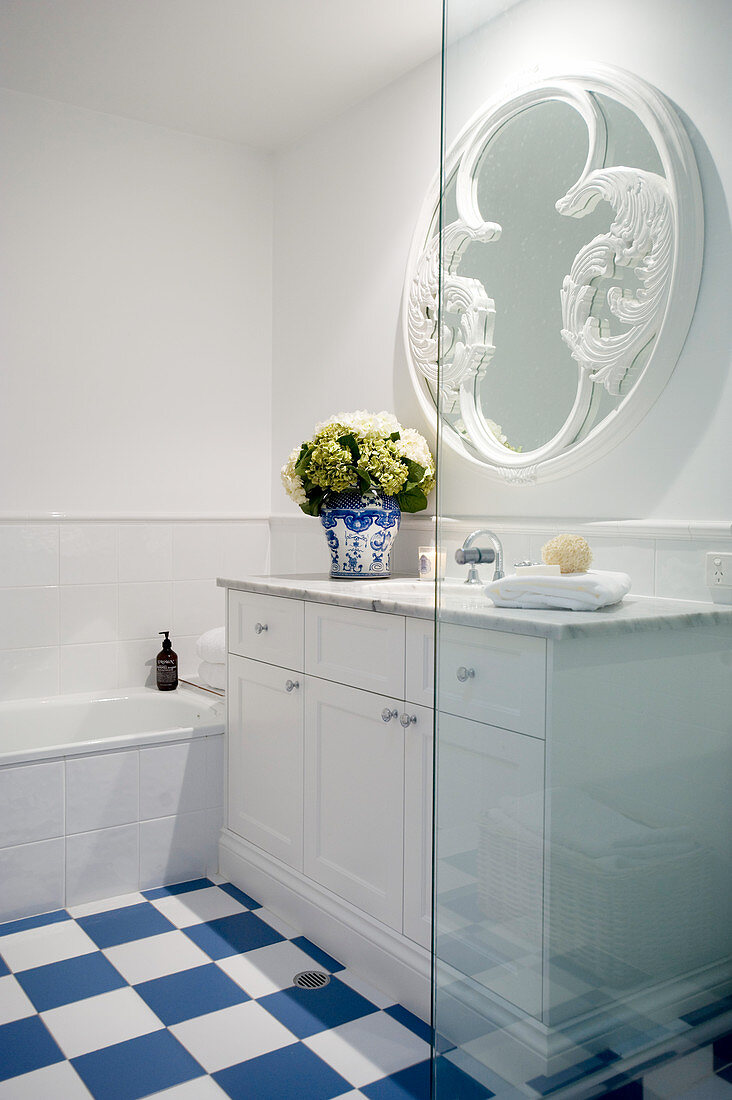 Washstand below round mirror in bathroom with blue-and-white floor tiles