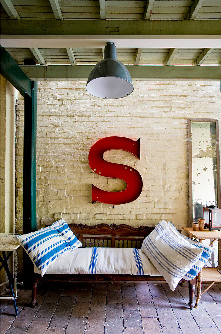Antique bench below large red letter S on brick wall on roofed terrace