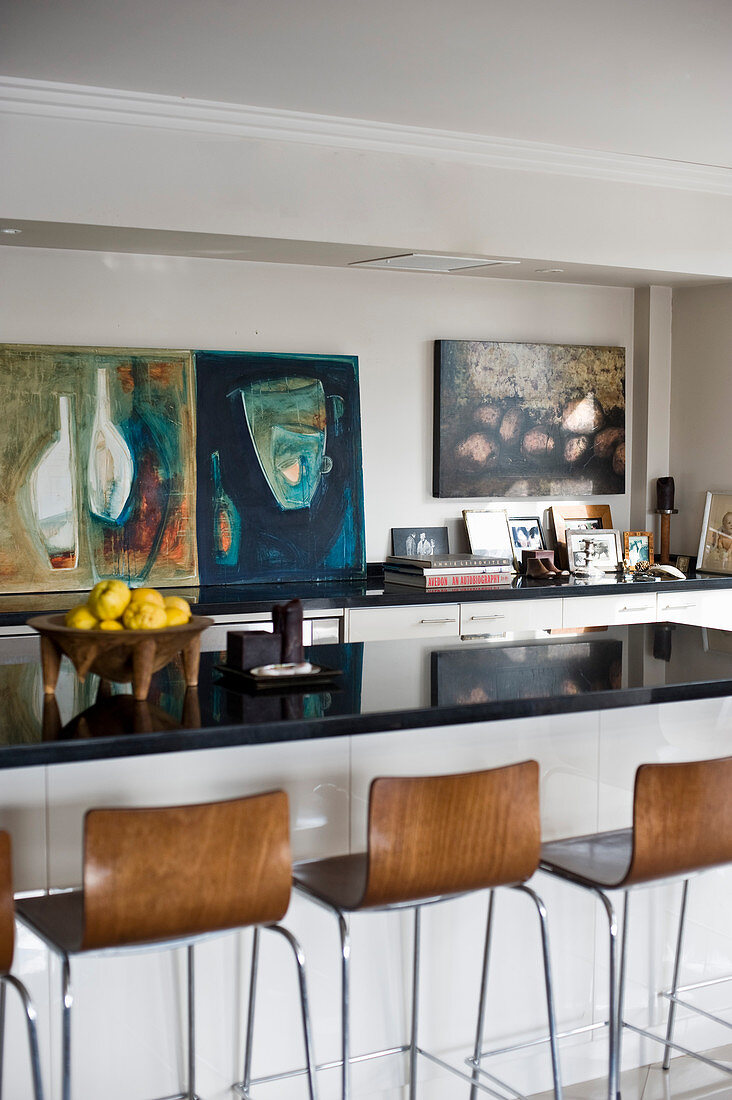 Barstools at breakfast bar of open-plan kitchen decorated with abstract paintings on walls