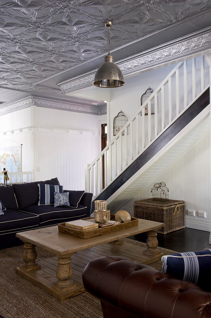 Rustikaler Couchtisch und Sofa im Wohnraum mit Treppe und silberfarbener Stuckdecke
