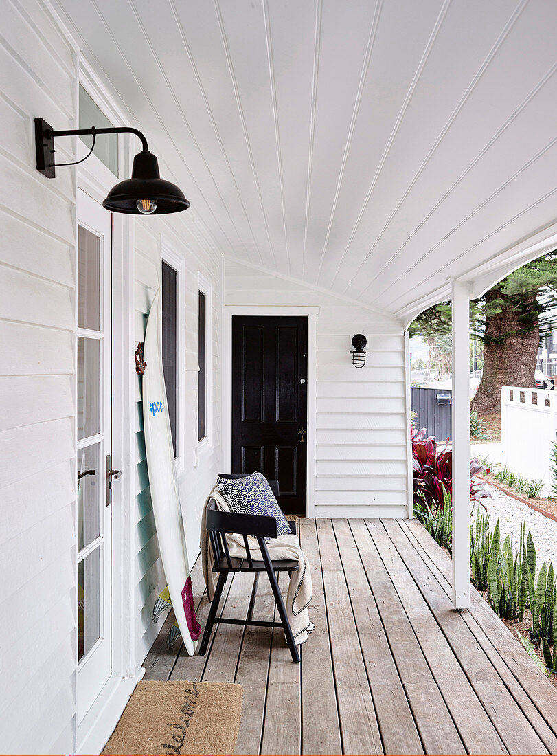Bench and surfboard on covered porch with white wood paneling