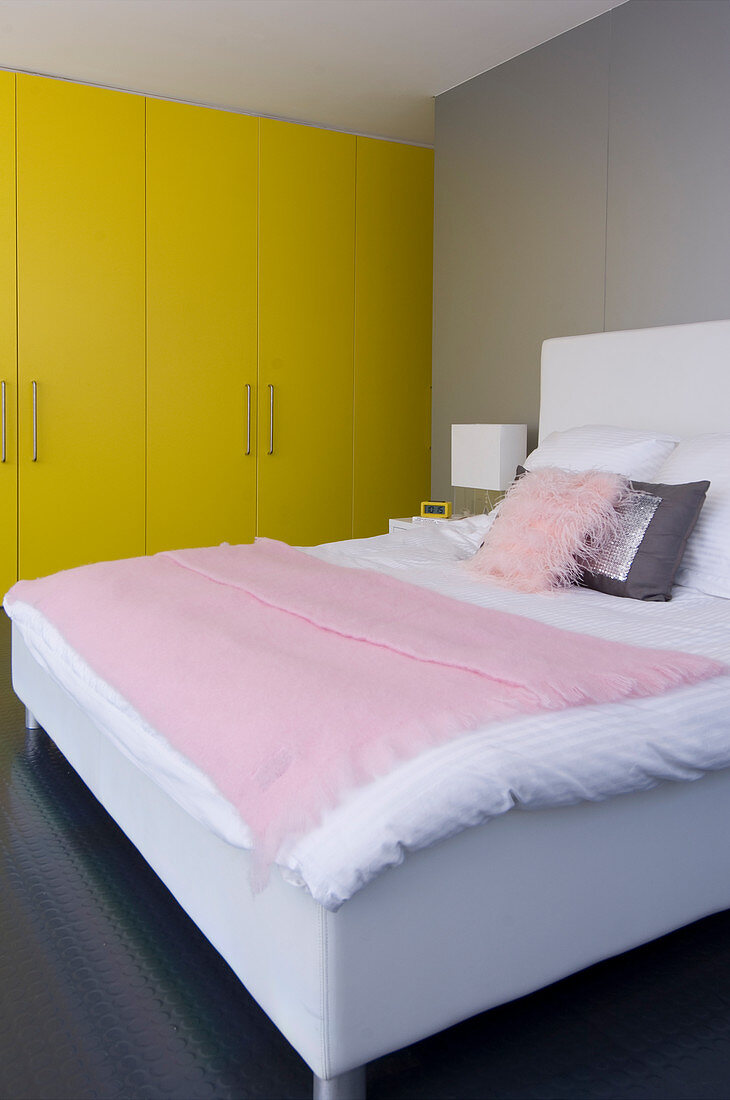 Gelbe Schrankwand und weißes Polsterbett mit rosa Bettdecke und Kissen in modernem Schlafzimmer