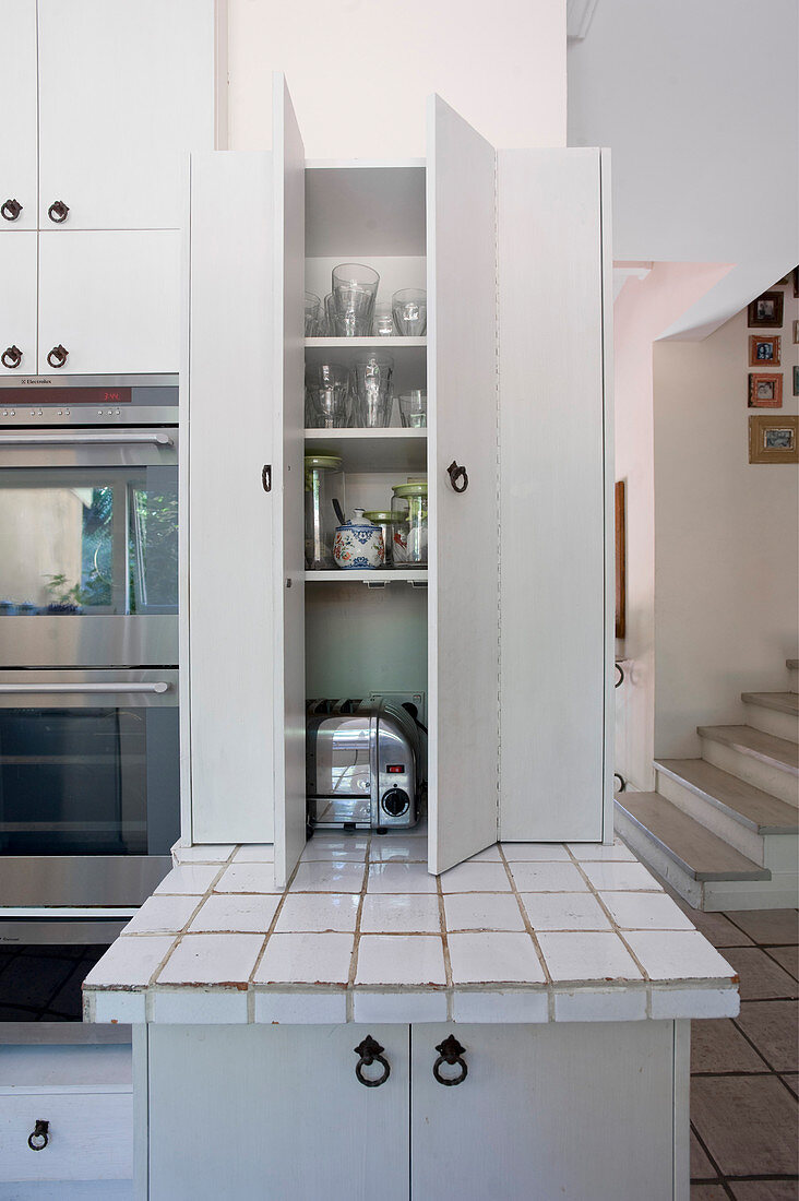 Geöffneter weißer Küchenschrank über gefliester Arbeitsplatte in Landhausküche