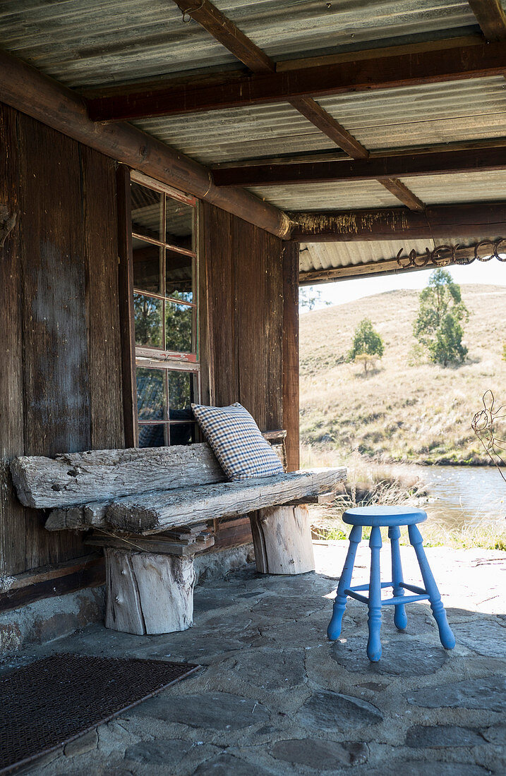Holzbank und Hocker auf überdachter Terrasse einer rustikalen Holzhütte
