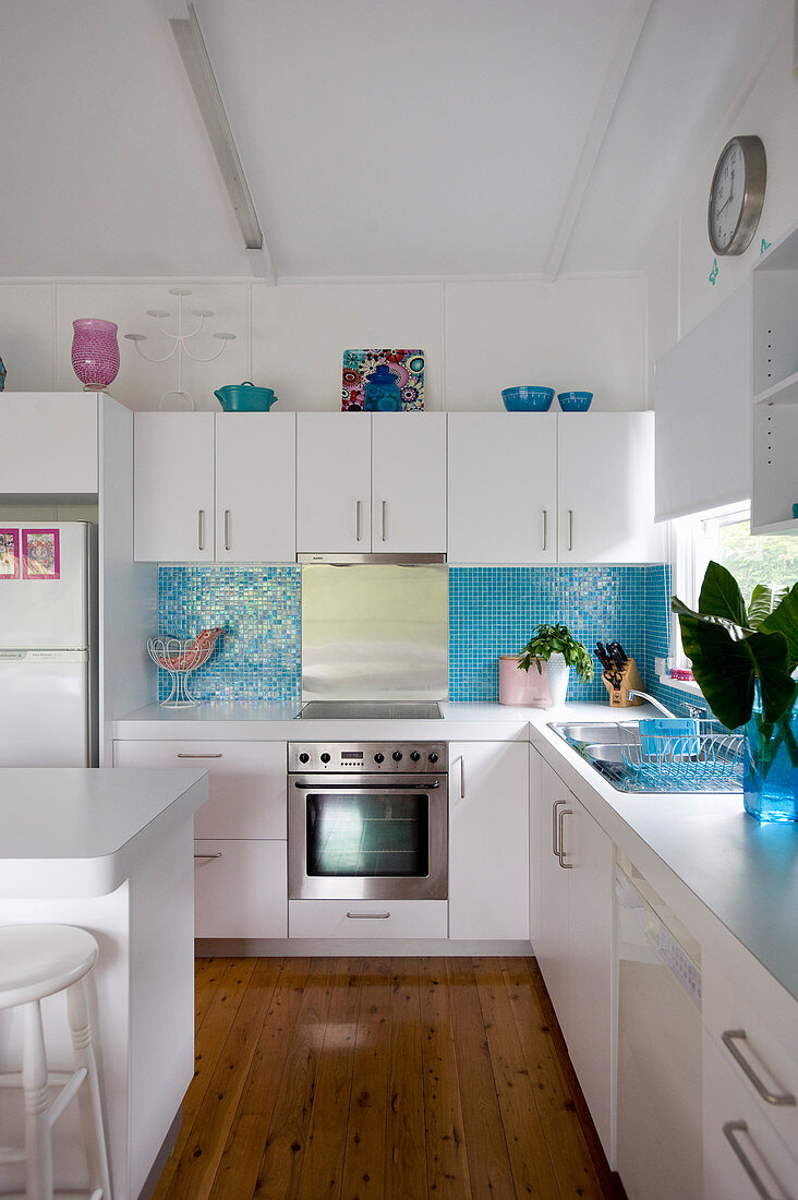 Küche mit weißen Küchenschränken und hellblauem Mosaikfliesenspiegel