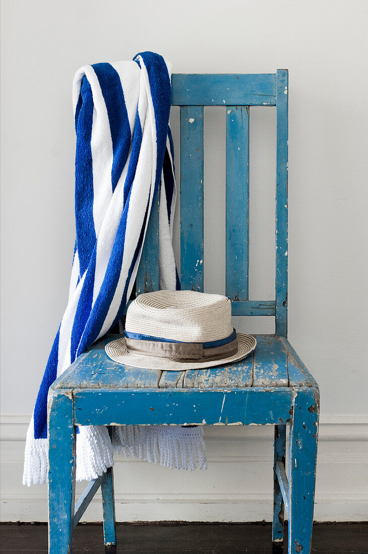 Hut und gestreiftes Badehandtuch auf blauem Vintage-Holzstuhl
