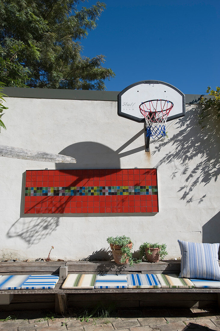Individuell gestalteter Innenhof mit Basketballkorb, Mosaikwandbild und flachen Holzsitzmöbeln